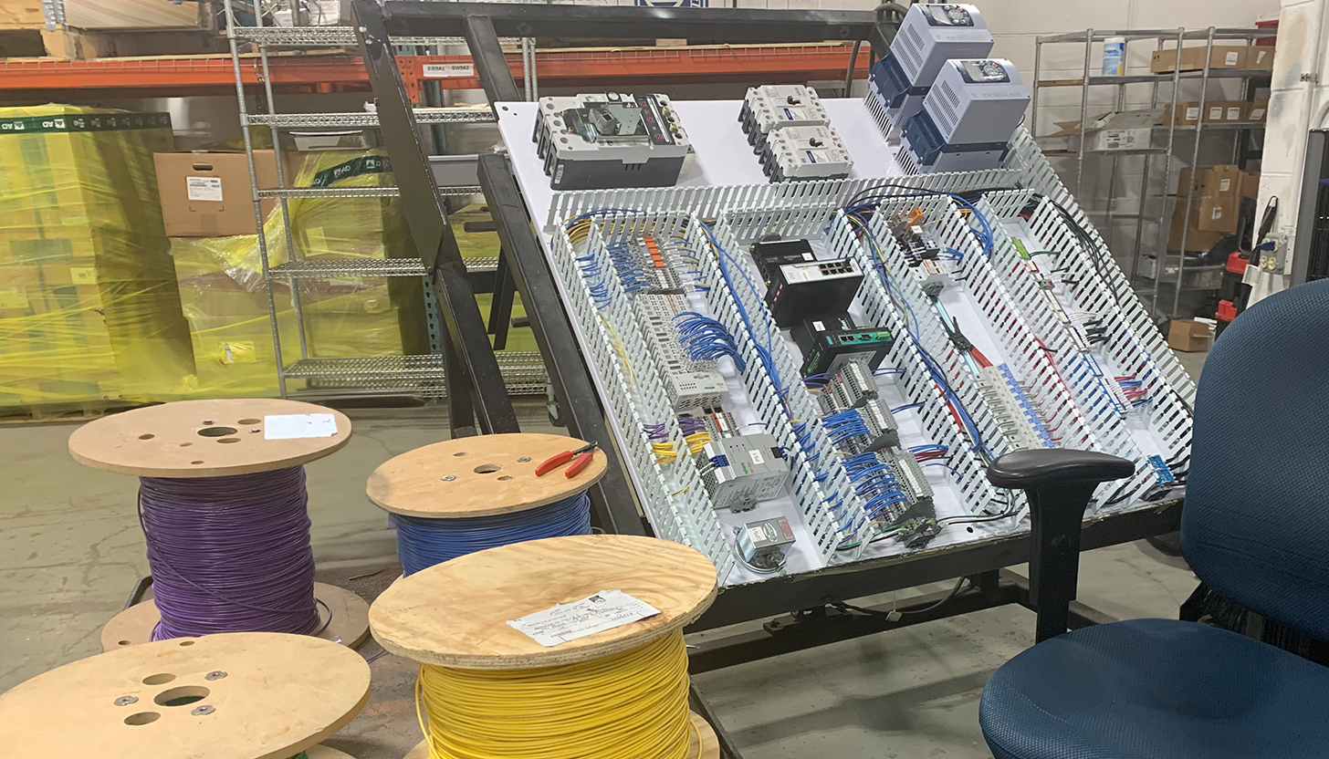 Industrial control panel in the process of assembly on a tilted table in Apex Industrial Automation's panel fabrication shop, with large rolls of colored wire in the foreground.
