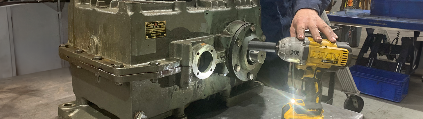 Mechanic at Apex Industrial Automation using a DeWalt power tool to disassemble a dirty gearbox on a lift table.