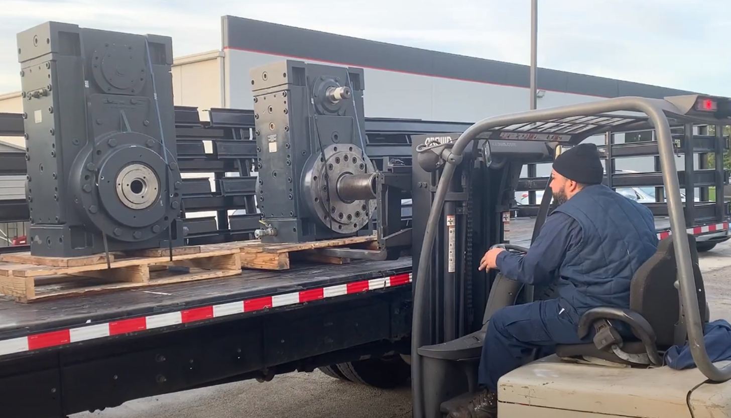 Two large repaired gearboxes being loaded onto an Apex Industrial Automation delivery truck by a forklift.