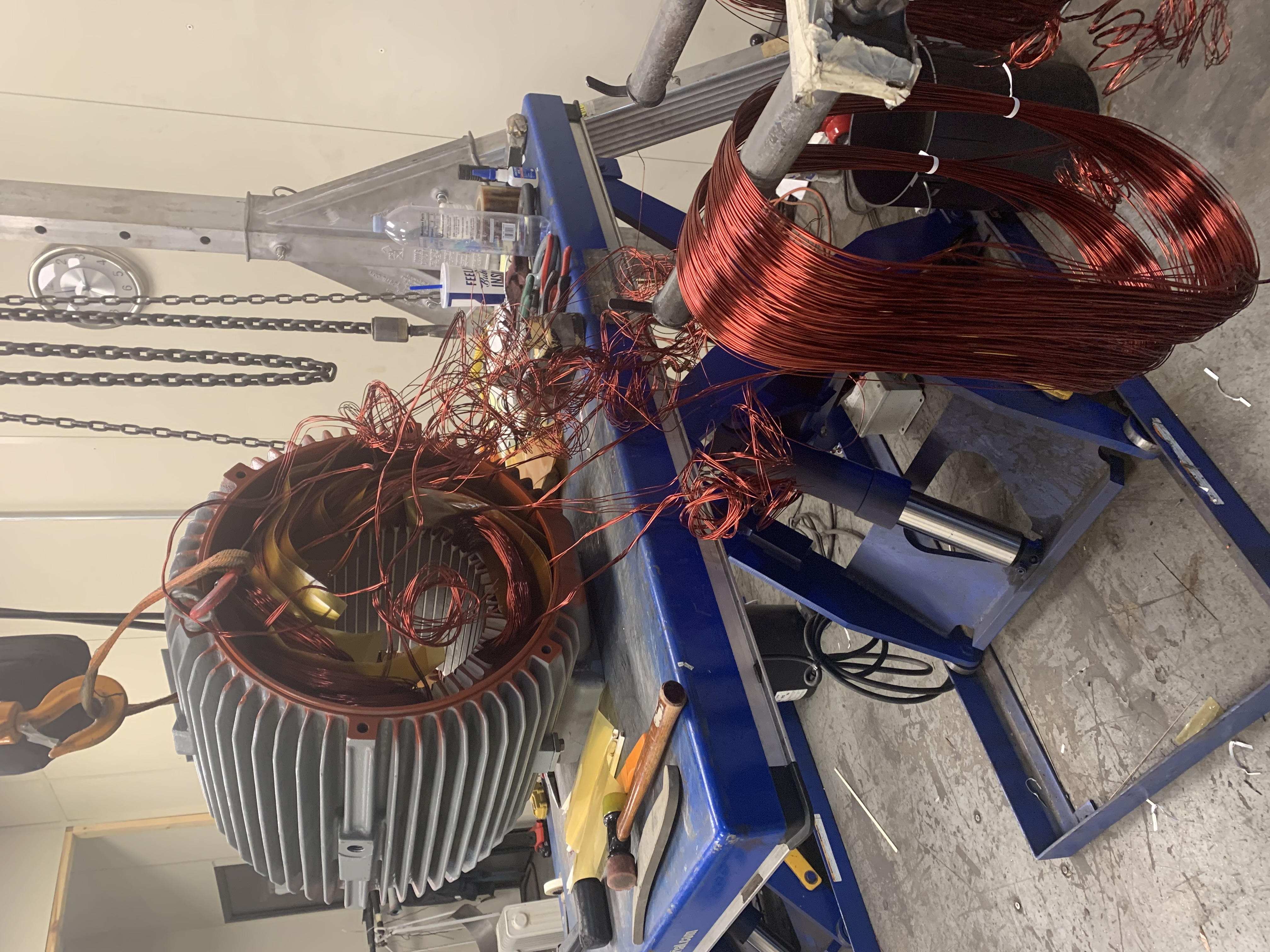 Electric motor rewind in progress at Apex Industrial Automation with a motor on a lift table connected to a gantry crane and wiring being woven into the stator.