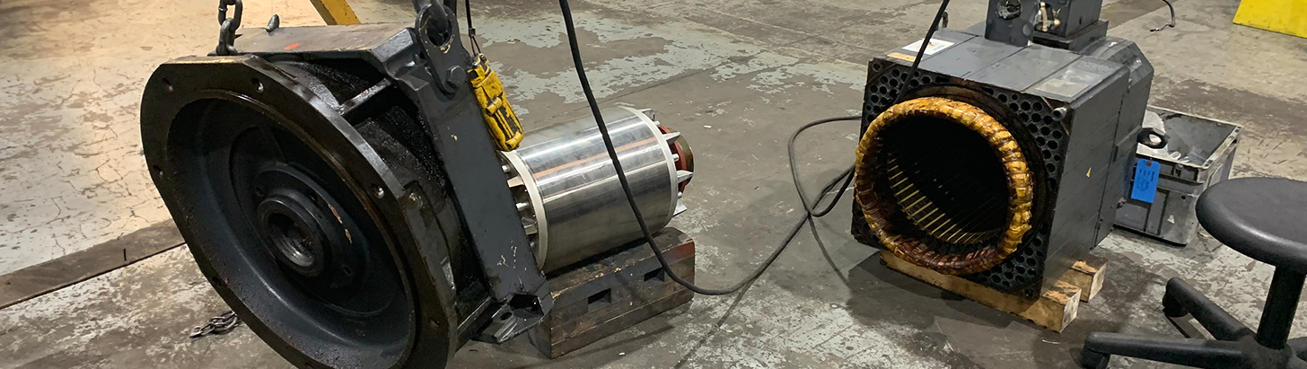 Large disassembled servo motor partially hanging from a gantry crane at Apex Industrial Automation.