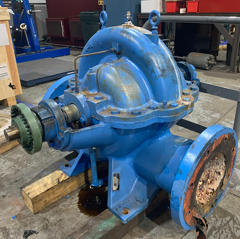 Blue water tower pump with a small leak on a pallet in Apex Industrial Automation's warehouse, awaiting repair.
