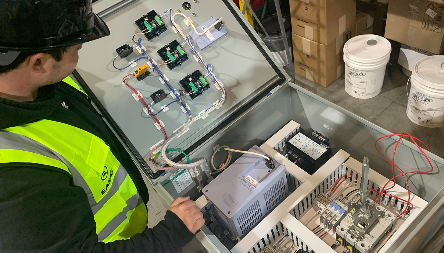 Apex Industrial Automation mechanic in branded safety vest and helmet finalizing their custom control panel fabrication.