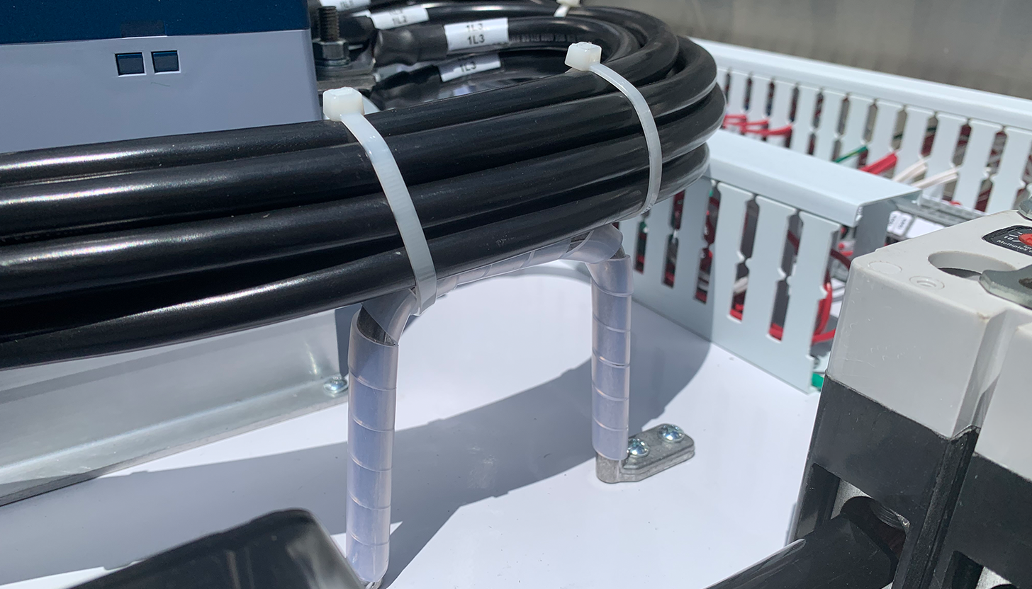 Close-up view inside a custom-made stainless steel dairy farm panel at Apex Industrial Automation, highlighting d-rings lifting high-voltage wires.