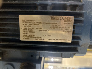 Close-up of an original SEW gearmotor nameplate before Apex Industrial Automation standardized the part number for DS Containers